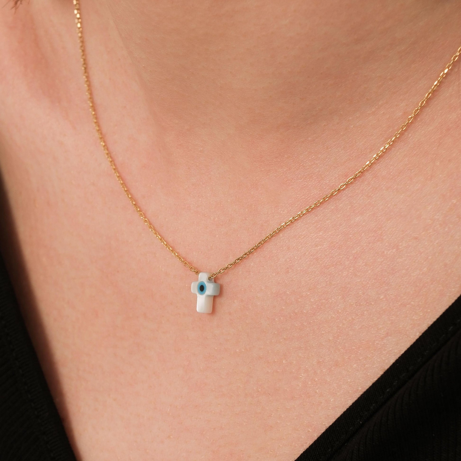 Angled shot of the 14K solid gold cross evil eye necklace resting gently on the skin, emphasizing the pendant&#39;s shine.