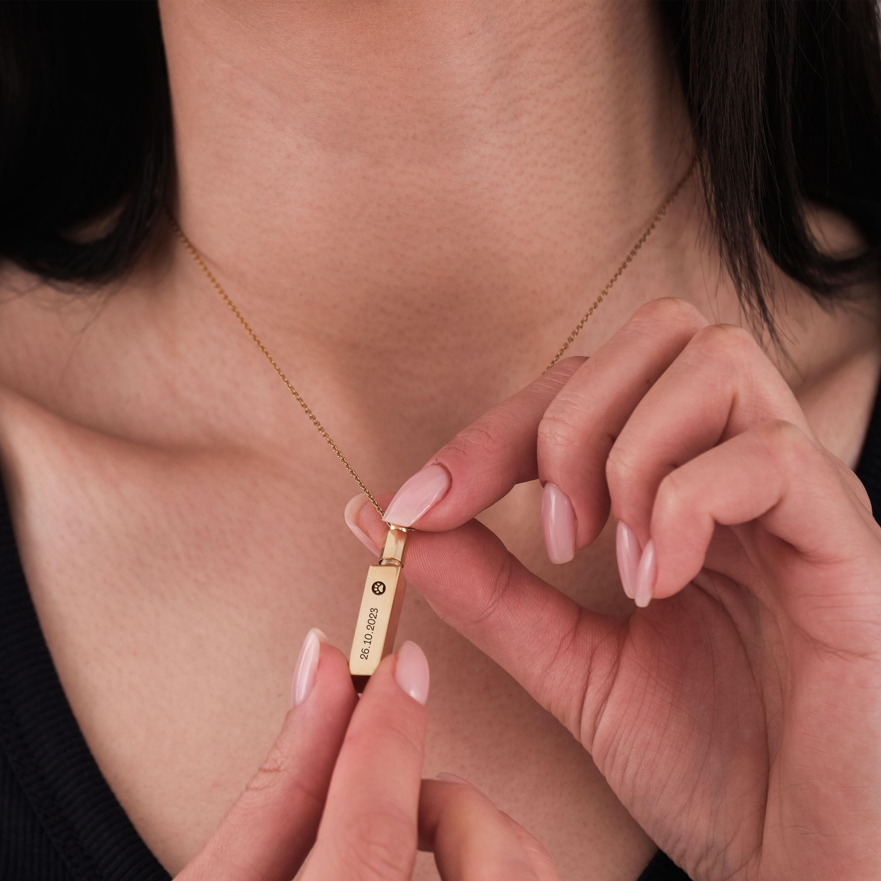 Woman holding 14K gold plated personalized cremation urn necklace near her neck.