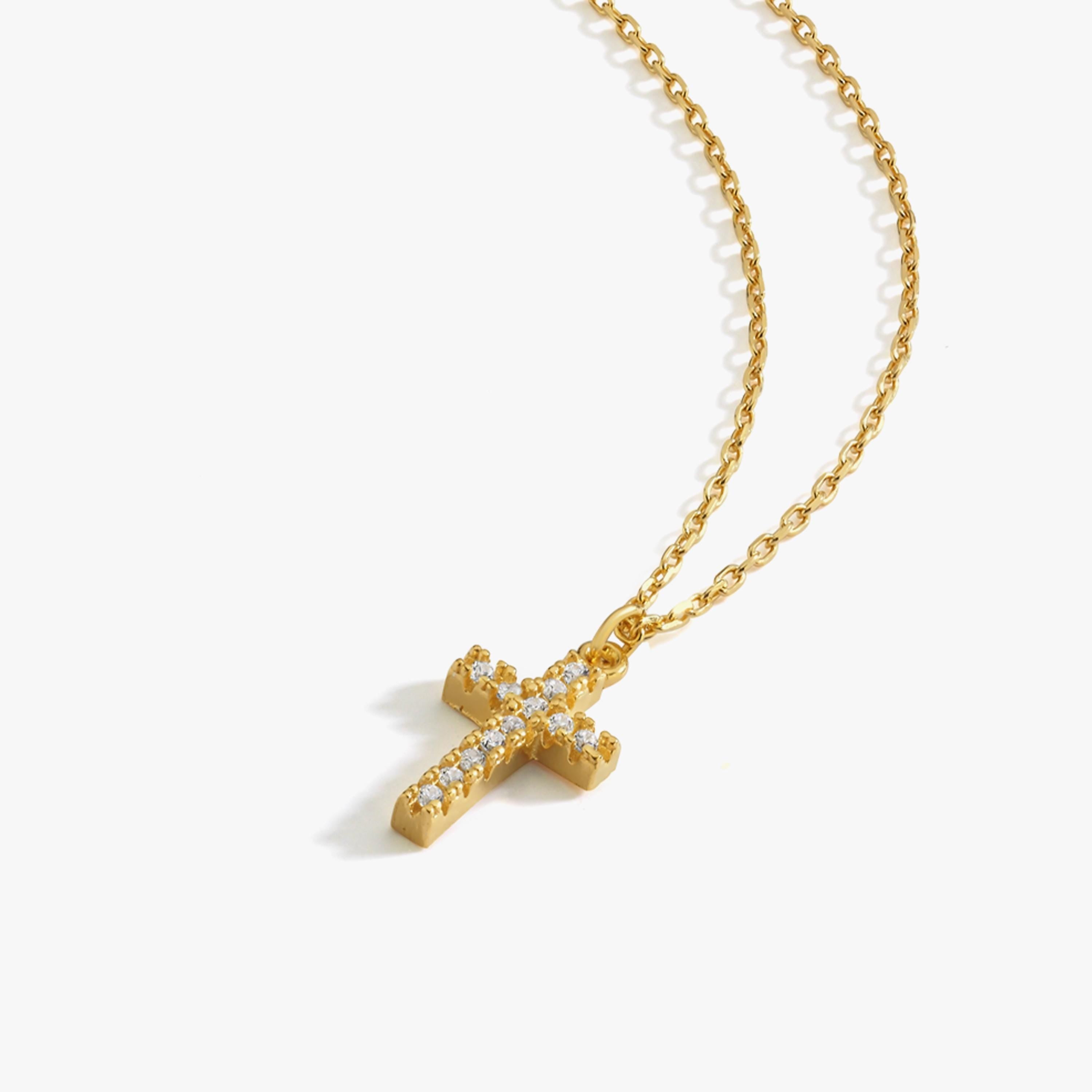 Studio image of an 18K gold vermeil cross necklace with sparkling white gemstones, laid flat on white background.