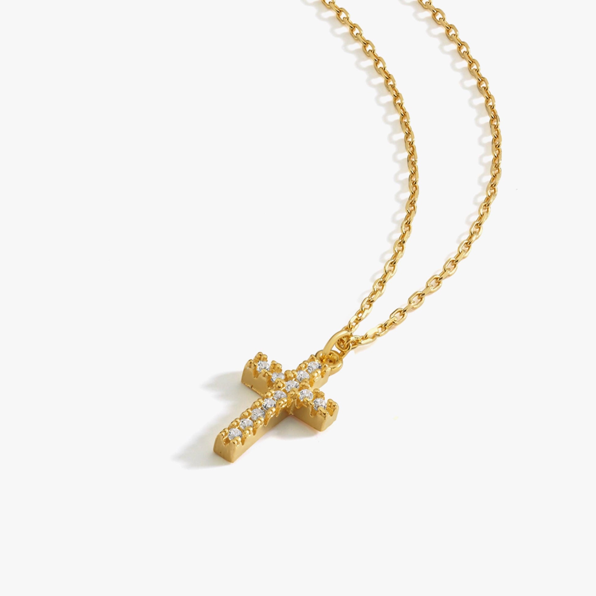 Studio image of an 18K gold vermeil cross necklace with sparkling white gemstones, laid flat on white background.