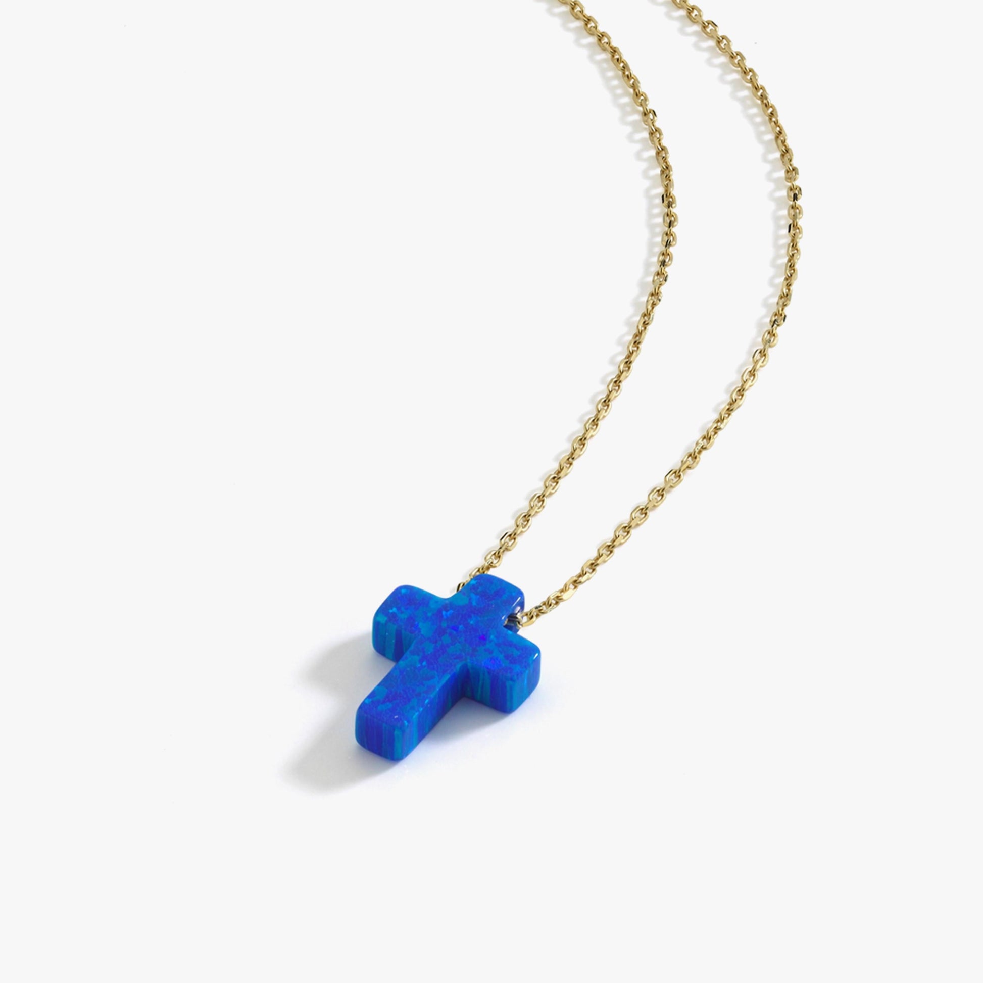 tudio shot of a 14K solid gold necklace with a polished blue opal cross pendant against a white background.