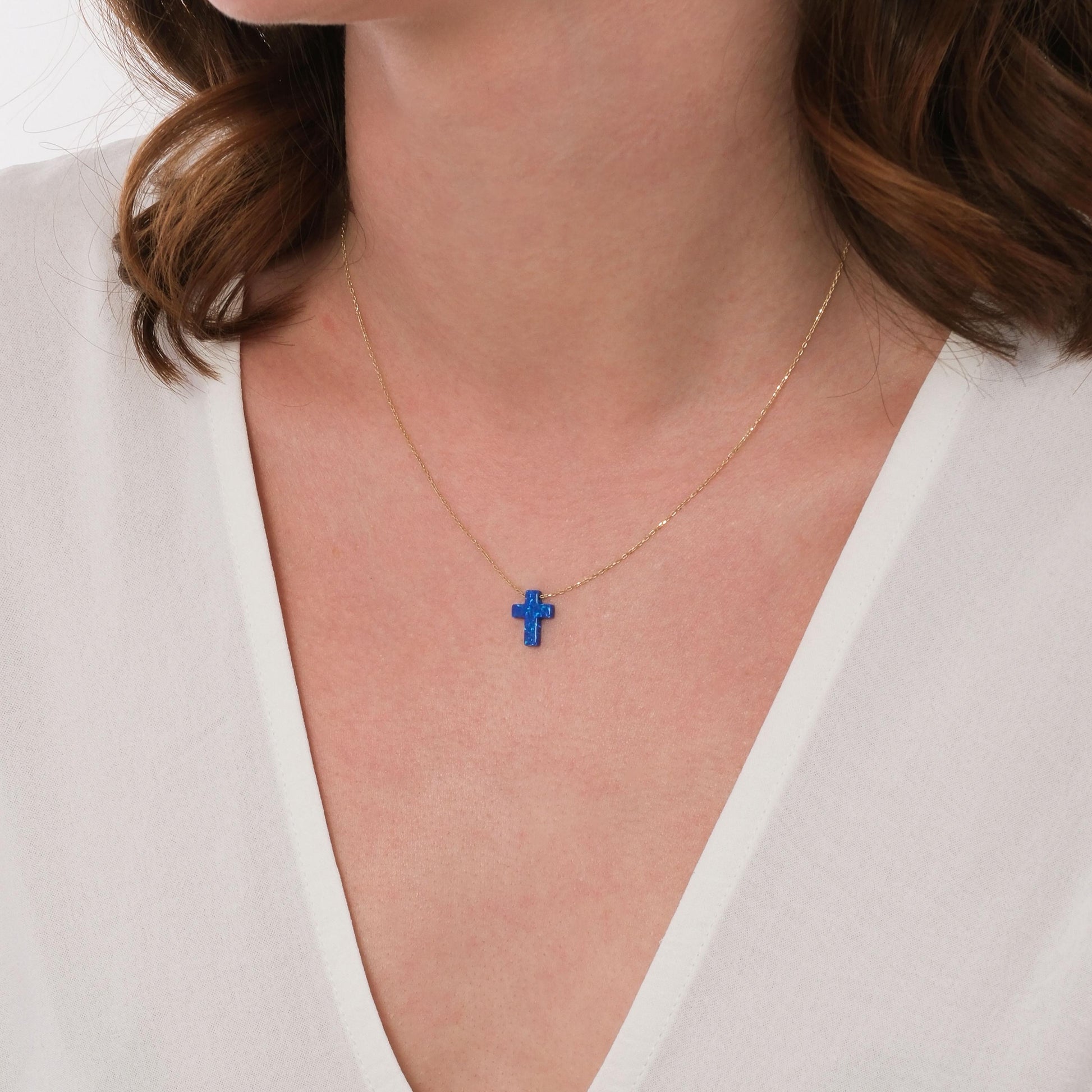 14K solid gold blue opal cross necklace worn over a white V-neck top.