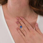 Close-up of a woman gently touching her 14K solid gold blue opal cross necklace.