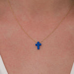 Close-up of a 14K solid gold necklace with a vibrant blue opal cross pendant resting at the center of the neck.