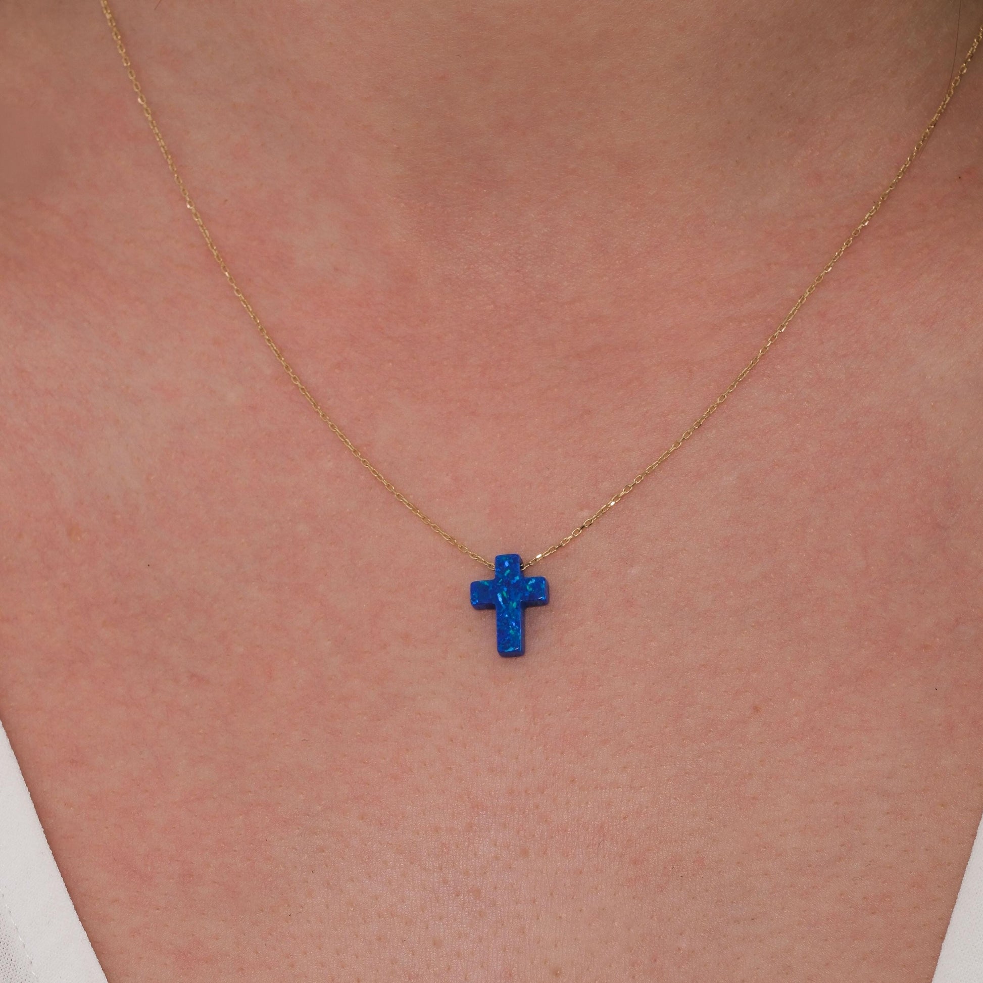 Close-up of a 14K solid gold necklace with a vibrant blue opal cross pendant resting at the center of the neck.