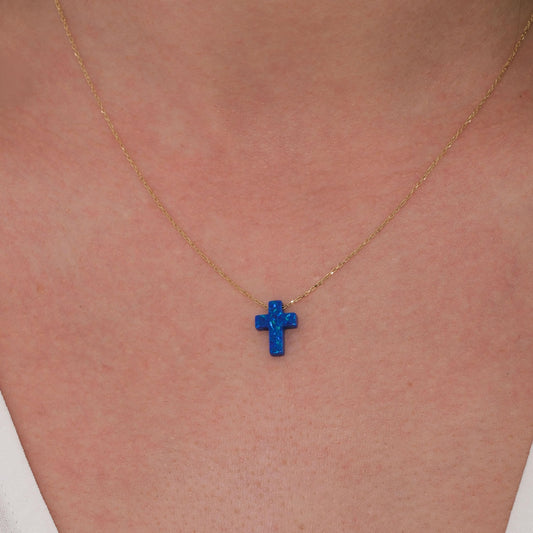 Close-up of a 14K solid gold necklace with a vibrant blue opal cross pendant resting at the center of the neck.