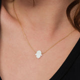 Minimal close-up showing the 14K solid gold opal Hamsa hand necklace resting at the center of the chest.