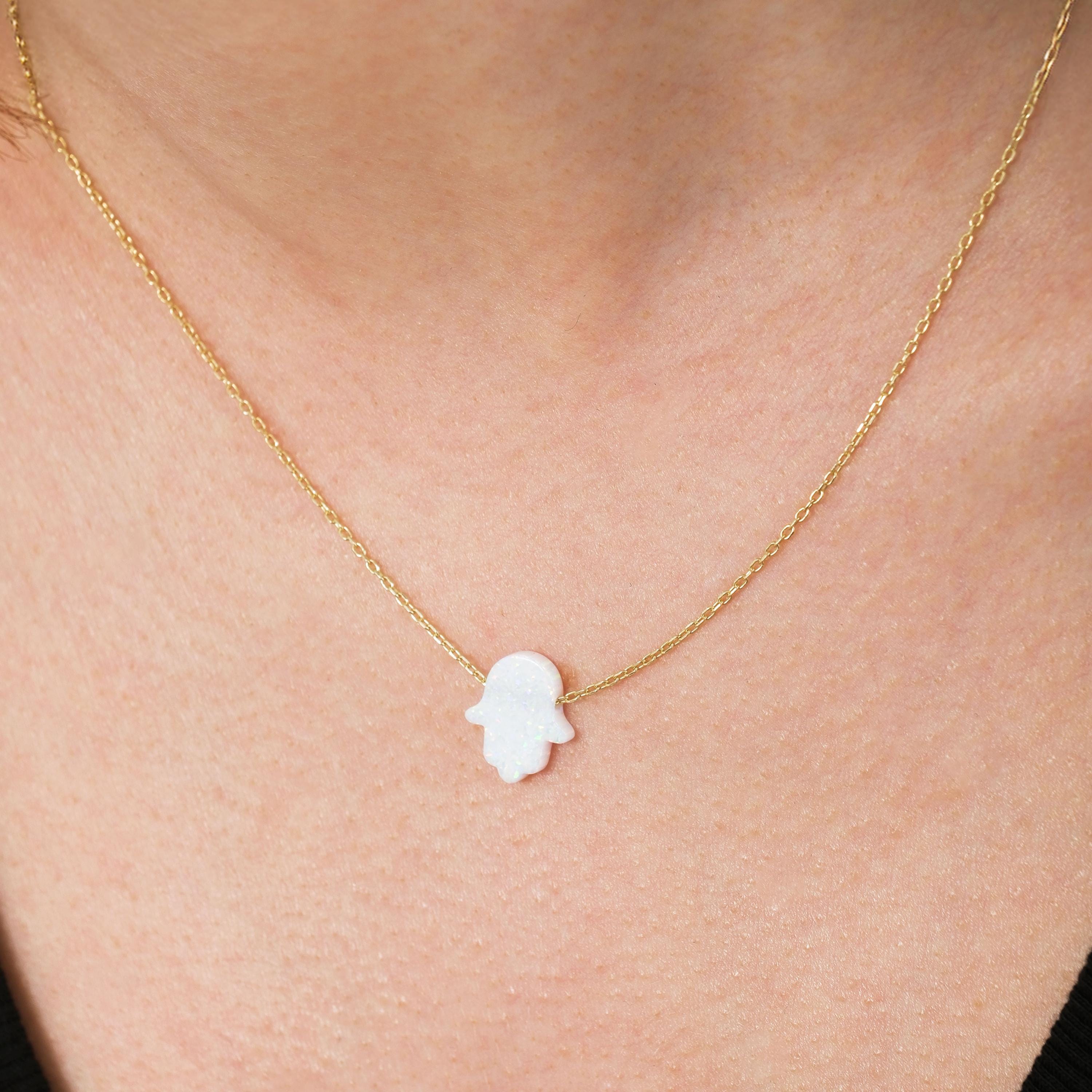 Detailed view of the 14K solid gold opal Hamsa hand necklace on the neck, with its delicate and luminous white opal centerpiece.
