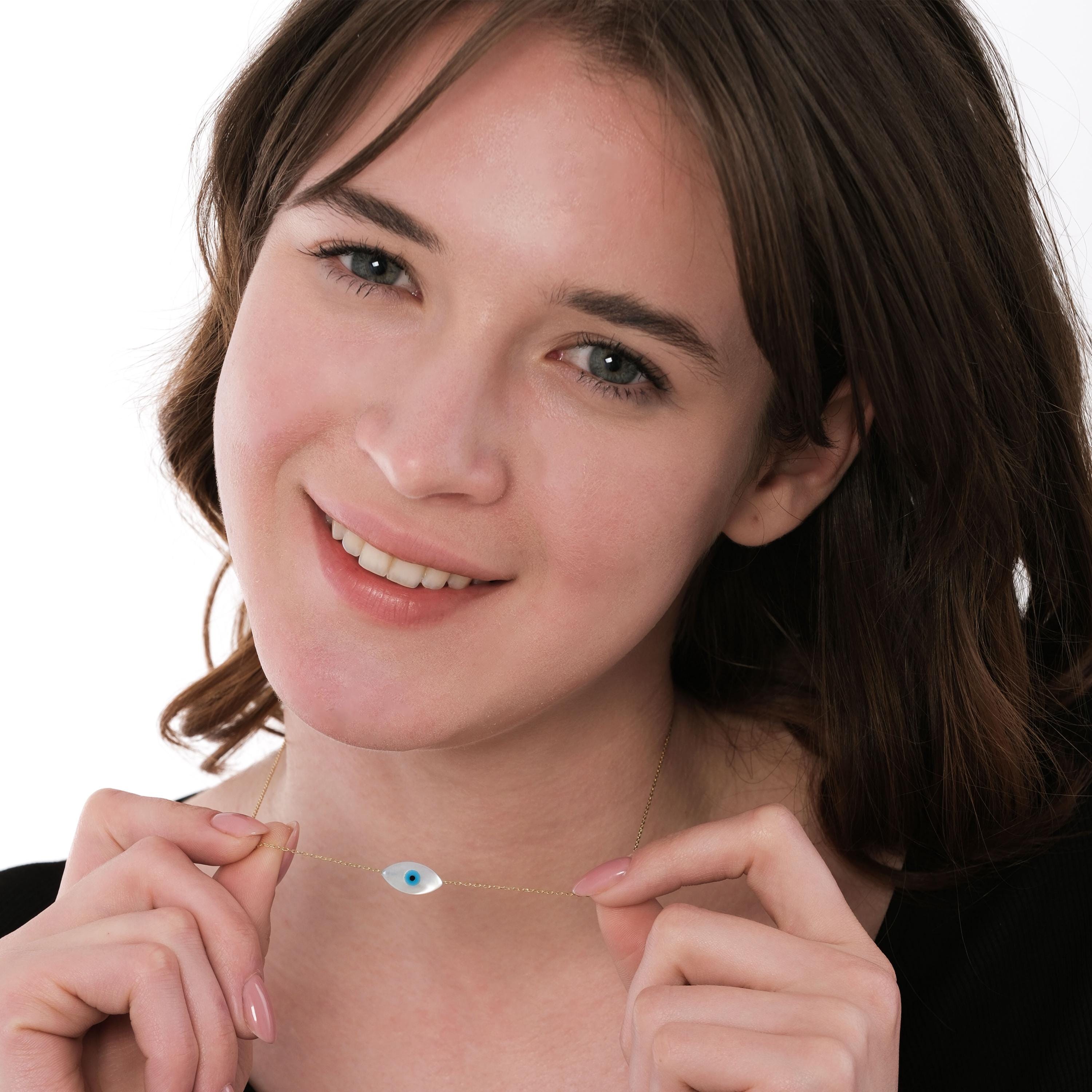 Smiling model holds and displays her 14K solid gold white opal necklace, showing the fine chain and centered charm.