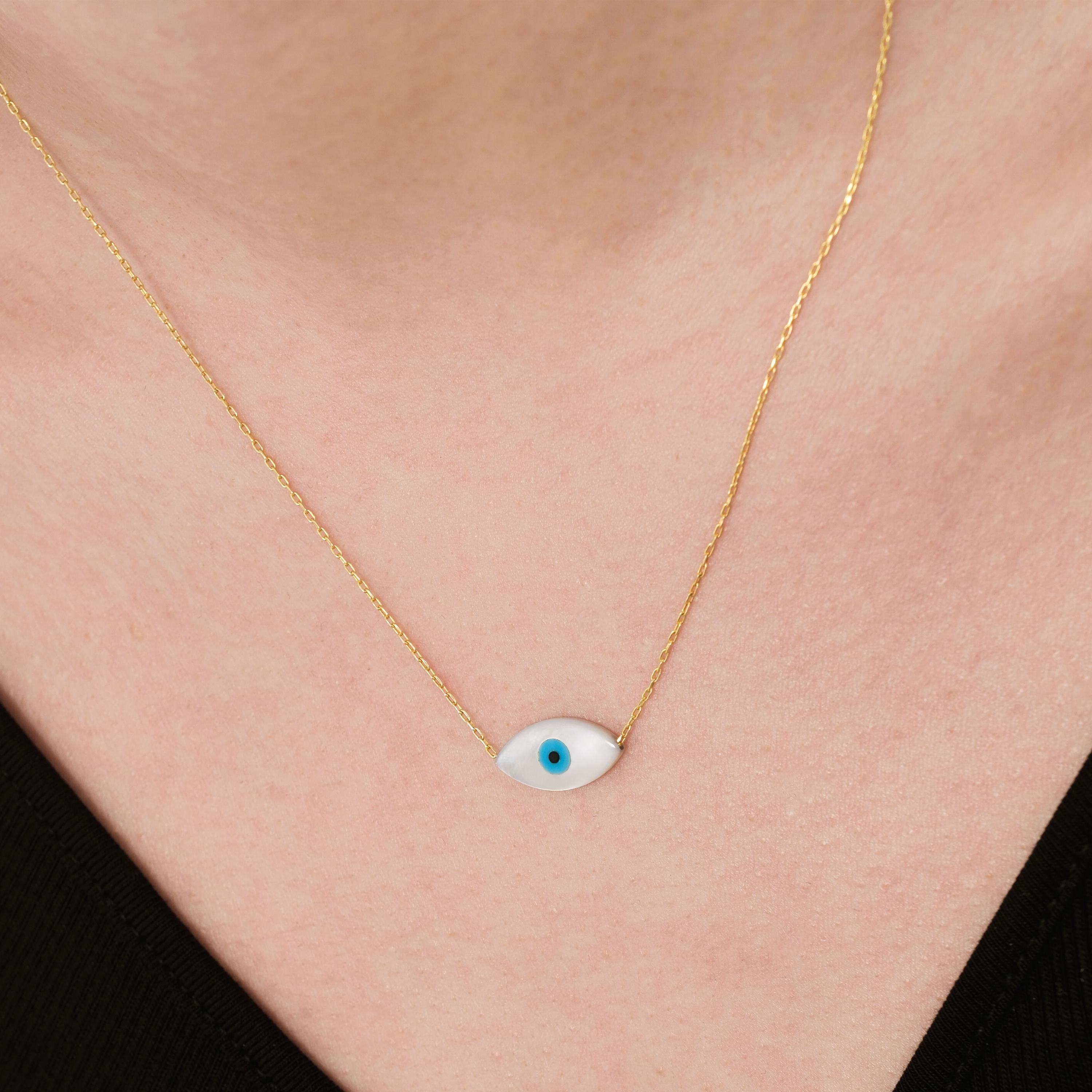 Close-up of a woman wearing a 14K solid gold white opal necklace featuring a sleek eye-shaped charm with a blue center.