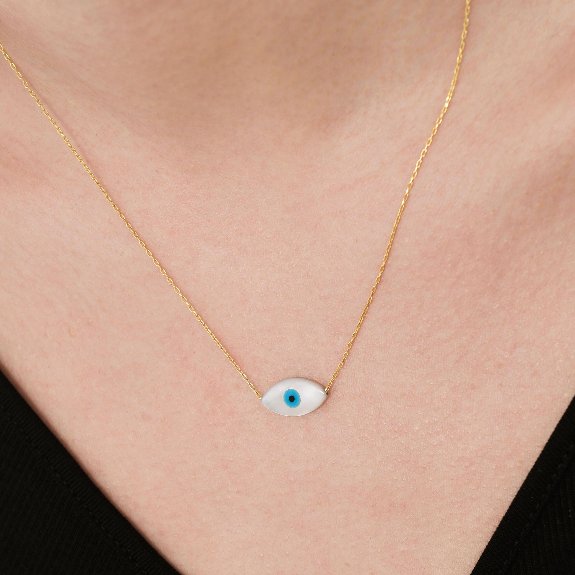 Close-up of a woman wearing a 14K solid gold white opal necklace featuring a sleek eye-shaped charm with a blue center.