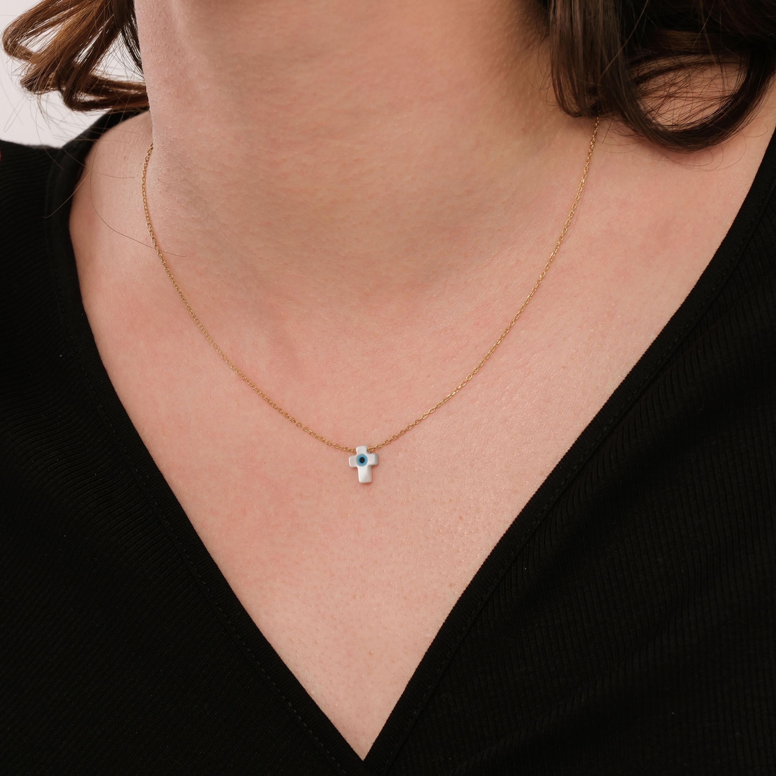 Minimalist image of the 14K solid gold cross evil eye necklace on the neck, styled with a simple black V-neck top.