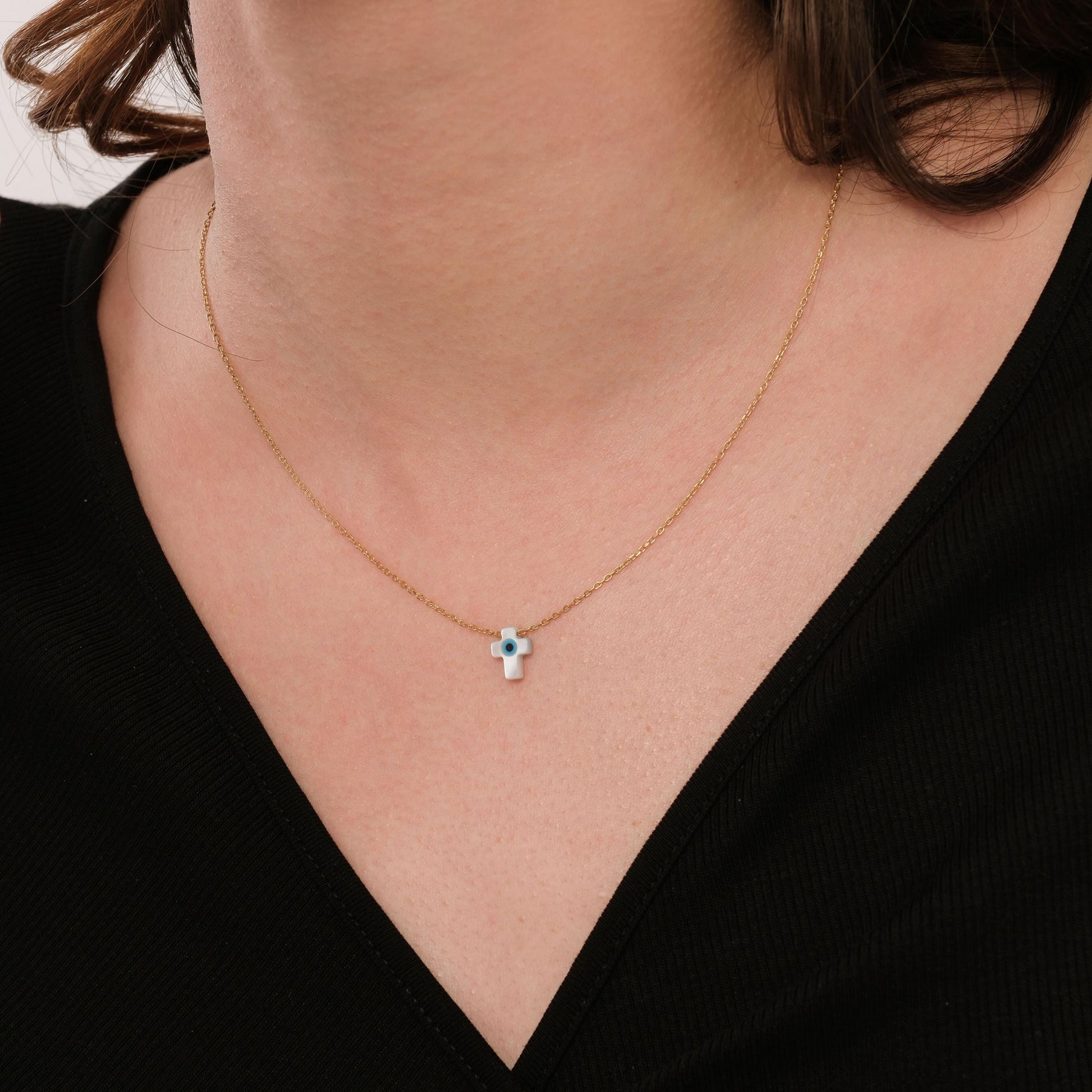 Minimalist image of the 14K solid gold cross evil eye necklace on the neck, styled with a simple black V-neck top.