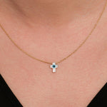 Close-up of a woman wearing a 14K solid gold cross evil eye necklace with a glossy white charm and a blue center.