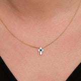 Close-up of a woman wearing a 14K solid gold cross evil eye necklace with a glossy white charm and a blue center.