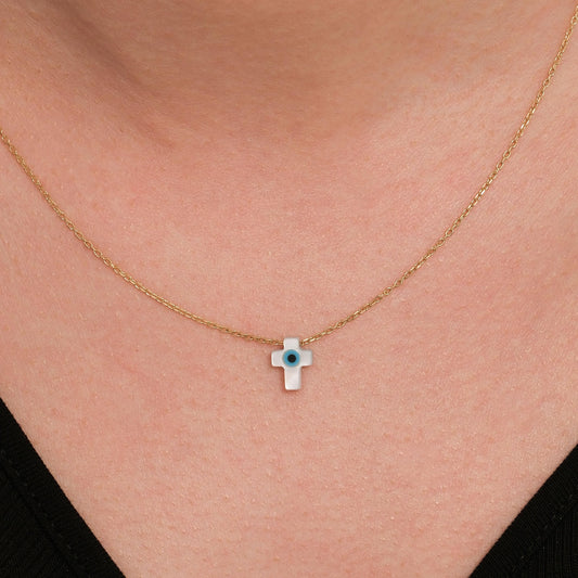 Close-up of a woman wearing a 14K solid gold cross evil eye necklace with a glossy white charm and a blue center.