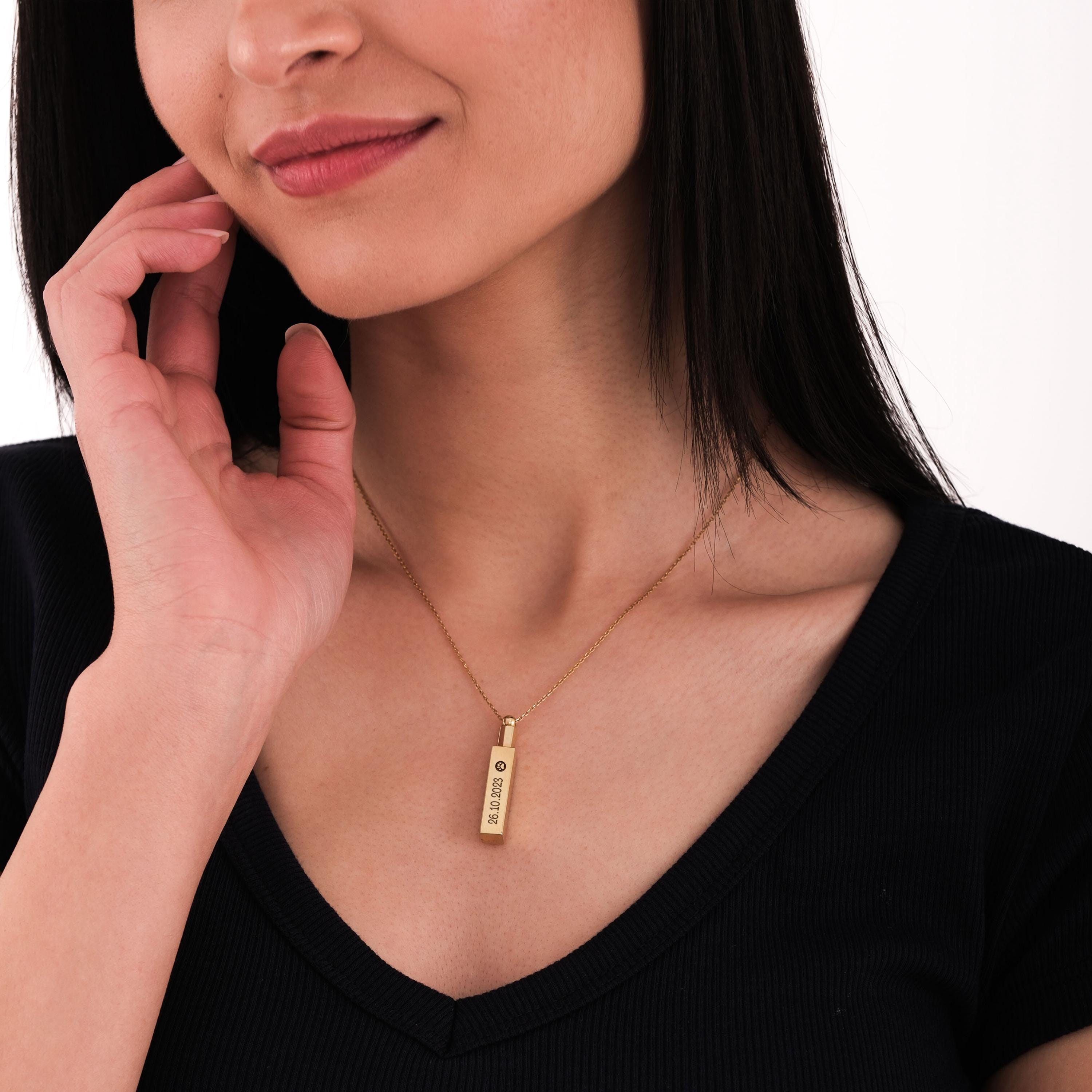 Smiling woman wearing 14K gold plated personalized cremation urn necklace over her chest.