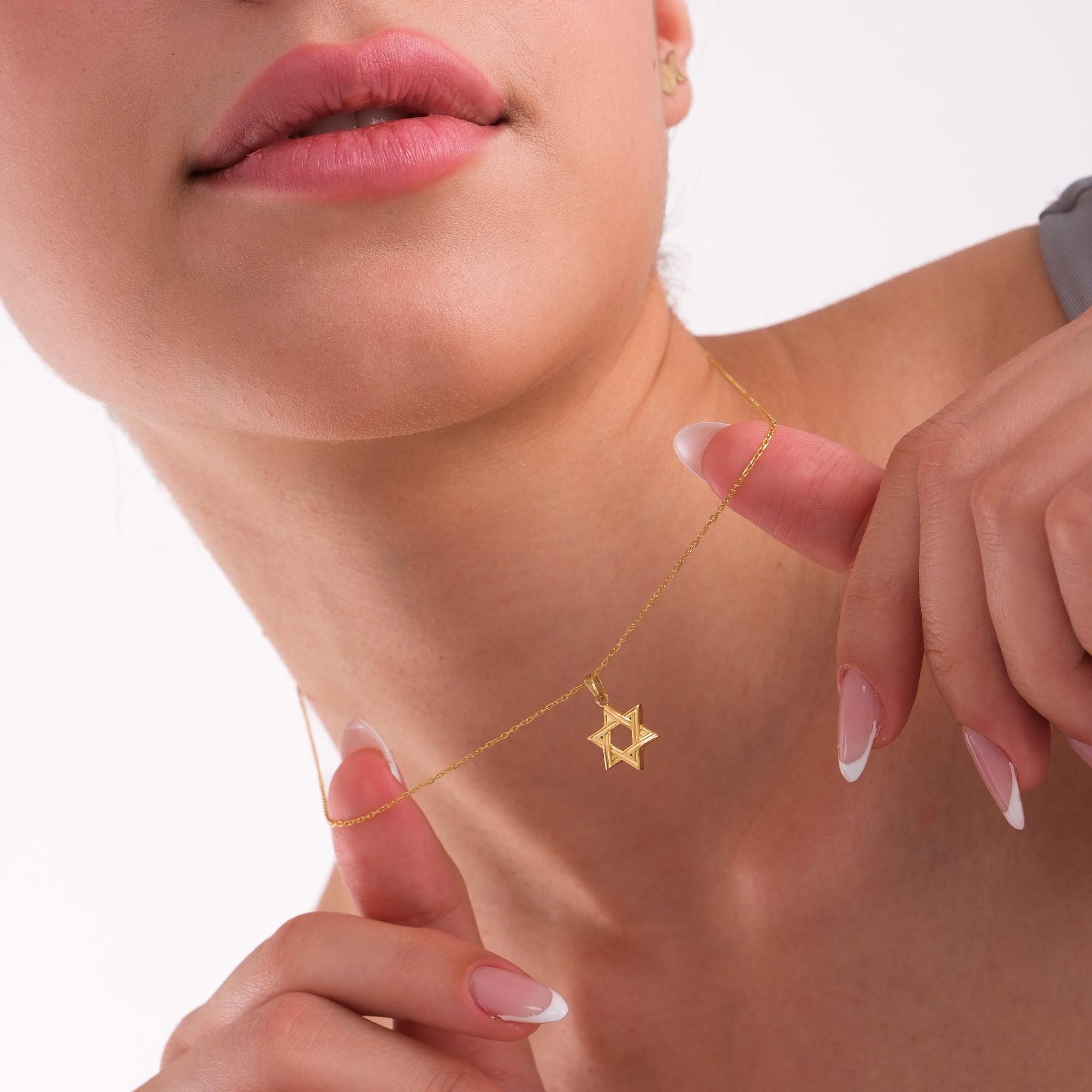 Woman holding a 14K Solid Gold Magen David Necklace close to her neck.