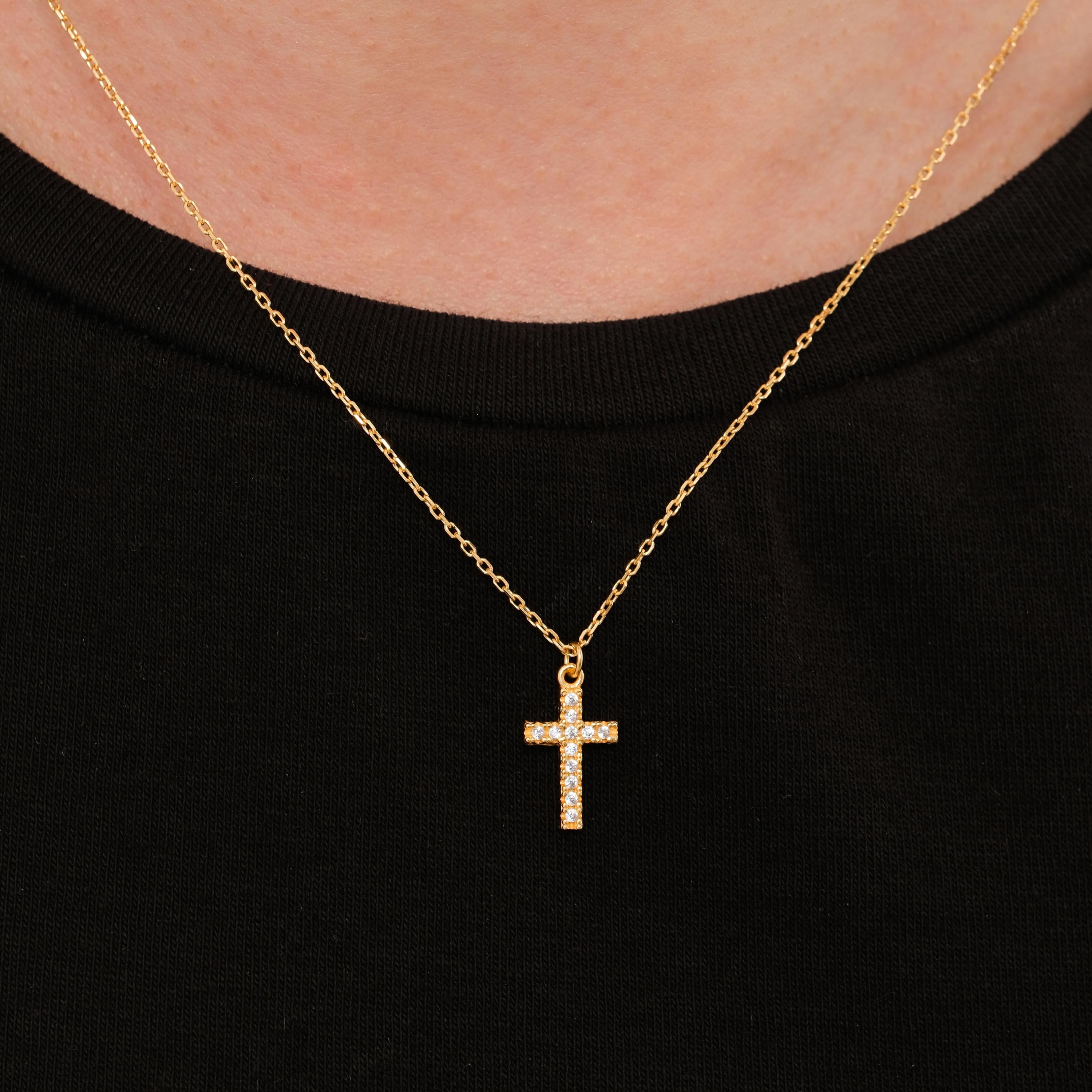 Clear gemstone cross necklace in 18K gold vermeil worn at the center of the neck on a black shirt.