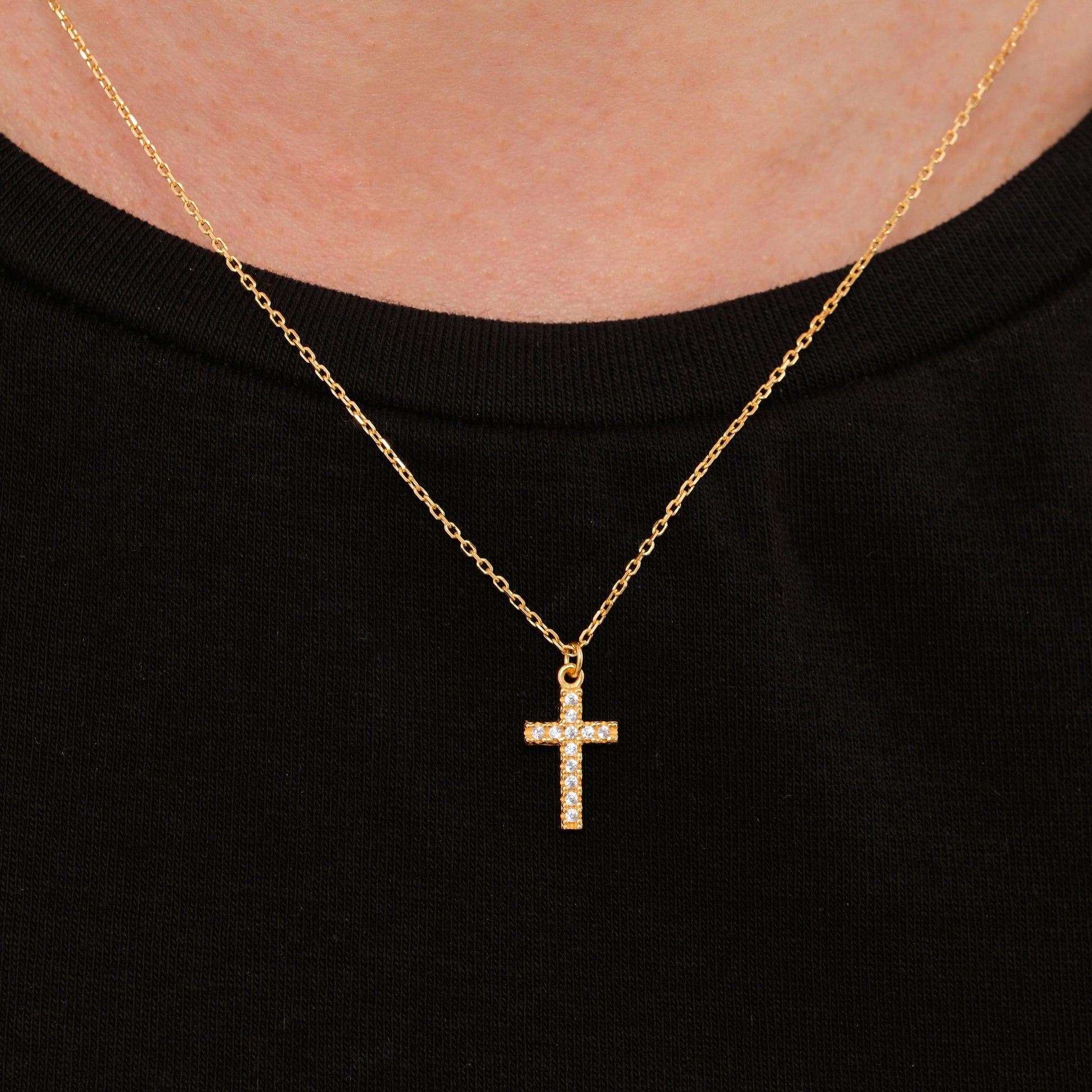 Clear gemstone cross necklace in 18K gold vermeil worn at the center of the neck on a black shirt.