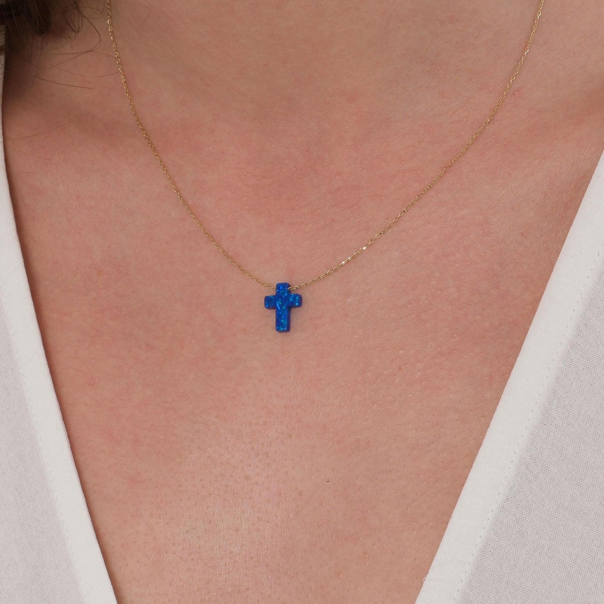 Zoomed view of a blue opal cross pendant necklace on a 14K solid gold chain, styled on the neck.