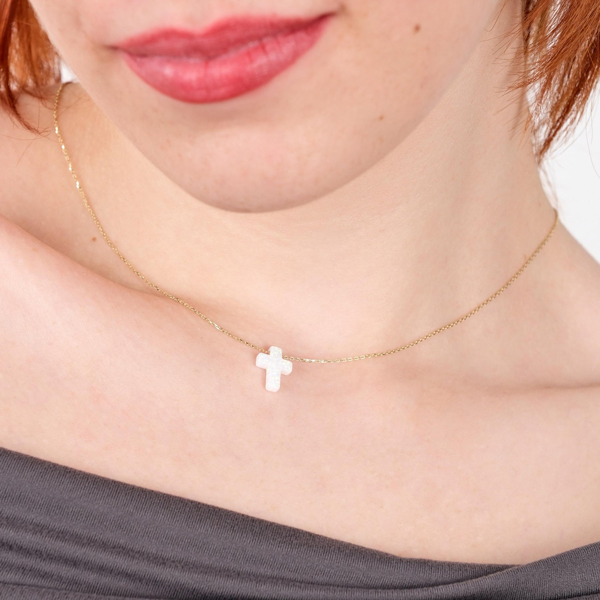 Close-up of a woman wearing a 14K solid gold white opal cross necklace, pendant resting just above the collarbone.