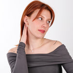 Woman posing in an off-shoulder gray top while wearing a 14K solid gold white opal cross necklace.