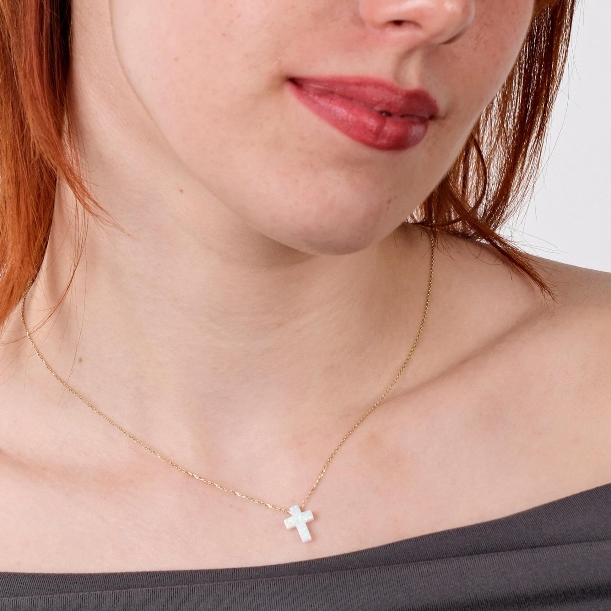 Woman wearing a 14K solid gold white opal necklace with a cross-shaped pendant, styled with an off-shoulder top.