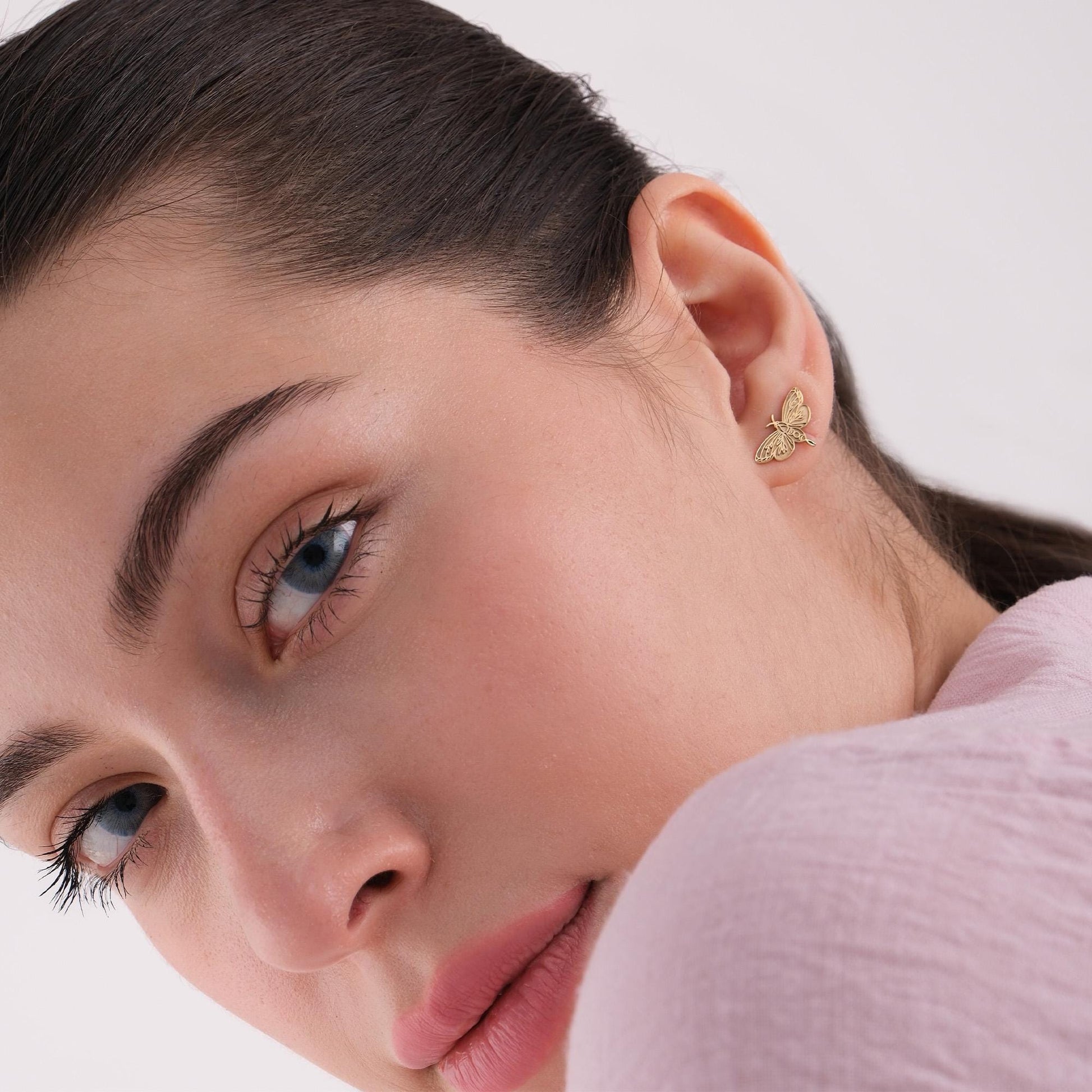 Portrait of a woman with blue eyes and 14K solid gold moth earrings, slightly tilting her head.