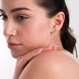 A woman in profile, resting her hand on her shoulder while displaying a 14K solid gold pentagram stud earring.