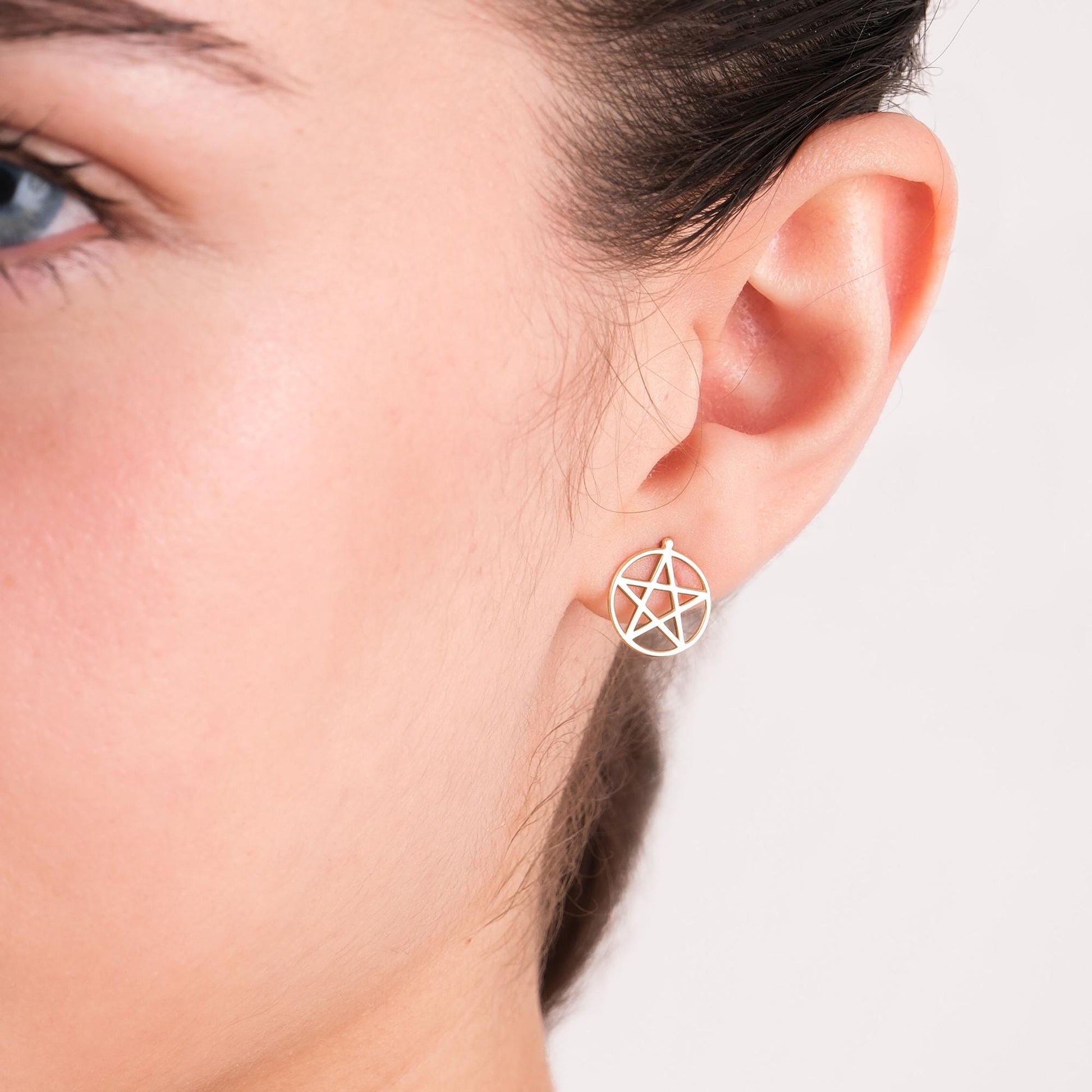 Close-up of a 14K solid gold pentagram stud earring worn on the left ear, showing the five-point star symbol.