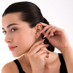 Portrait of a woman in a black top adjusting her 14K solid gold Witches Knot earrings, emphasizing their mystical and elegant appeal.