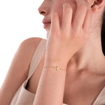 Side portrait of a woman showing off a 14K solid gold cross bracelet with diamonds, worn with a neutral-toned dress.