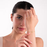 Smiling woman showcasing a 14K solid gold cross bracelet with central diamonds, worn on her raised wrist.