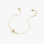 Minimalist 14K solid gold cross bracelet for women with central diamond cluster, displayed diagonally on white background.