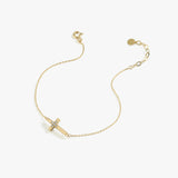 Minimalist 14K solid gold cross bracelet for women with central diamond cluster, displayed diagonally on white background.
