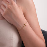 Woman wearing a 14K solid gold dainty cross bracelet with a bold, polished cross charm resting on her wrist.