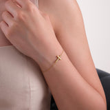 Woman wearing a 14K solid gold dainty cross bracelet with a bold, polished cross charm resting on her wrist.