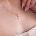 Close-up of a 14K solid gold Ankh necklace resting on a woman’s collarbone, styled with a deep V-neck top.