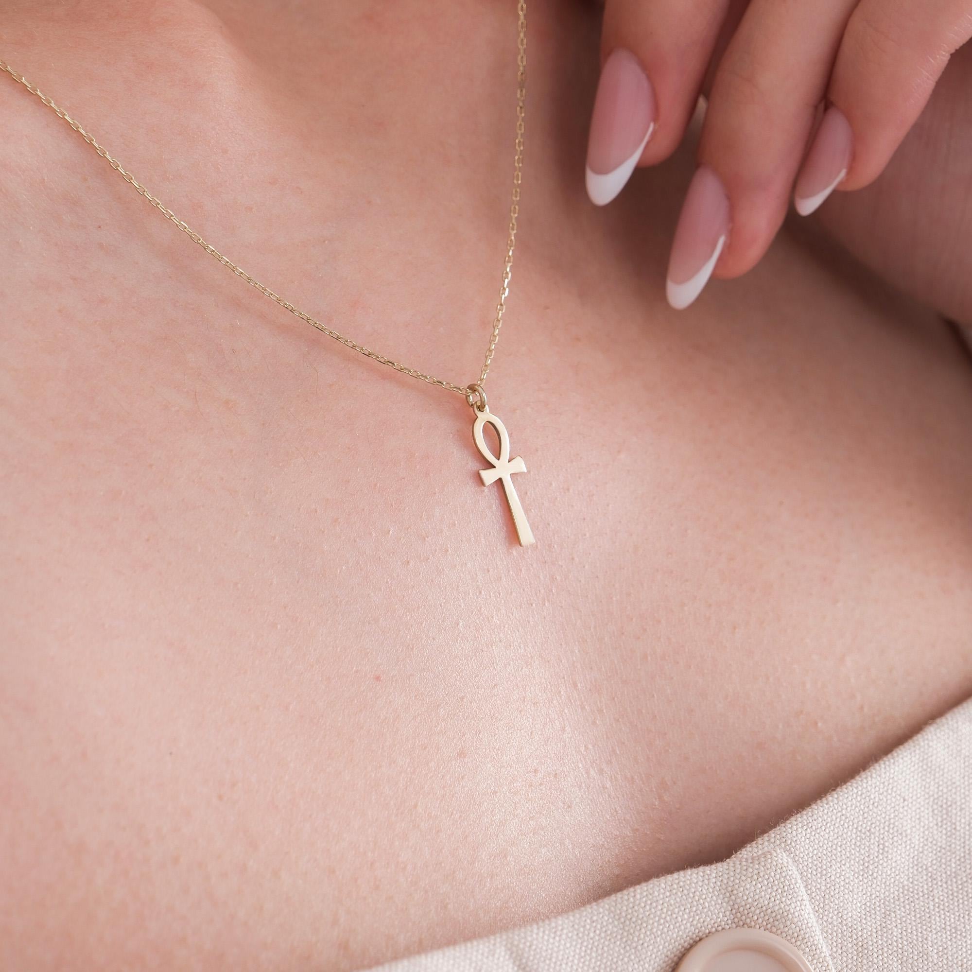 Close-up of a 14K solid gold Ankh necklace resting on a woman’s collarbone, styled with a deep V-neck top.