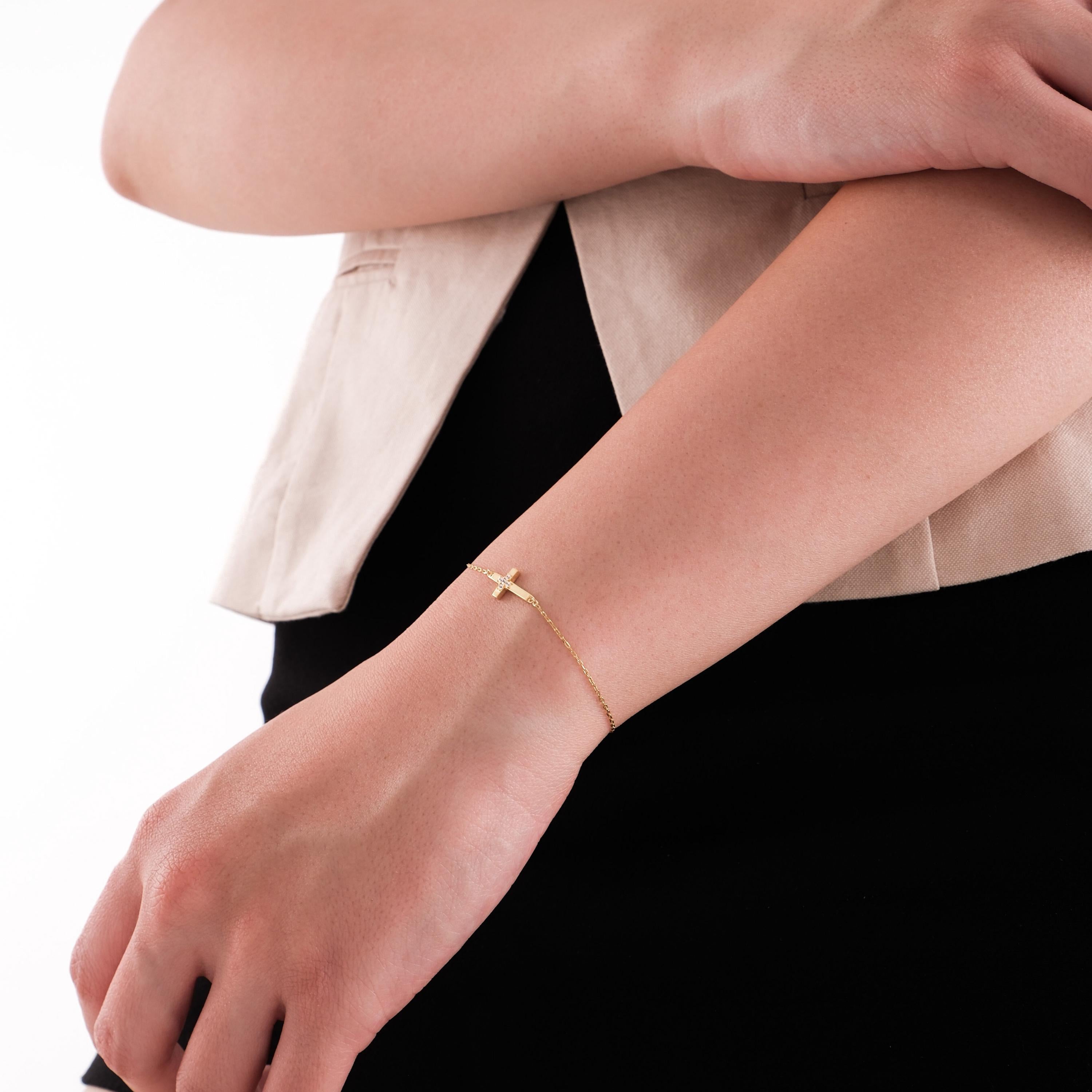 Model crossing arms while wearing a 14K solid gold cross bracelet for women, with shimmering diamond details.