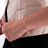 Woman wearing a 14K solid gold cross bracelet with diamond accents, styled elegantly over a beige blazer sleeve.