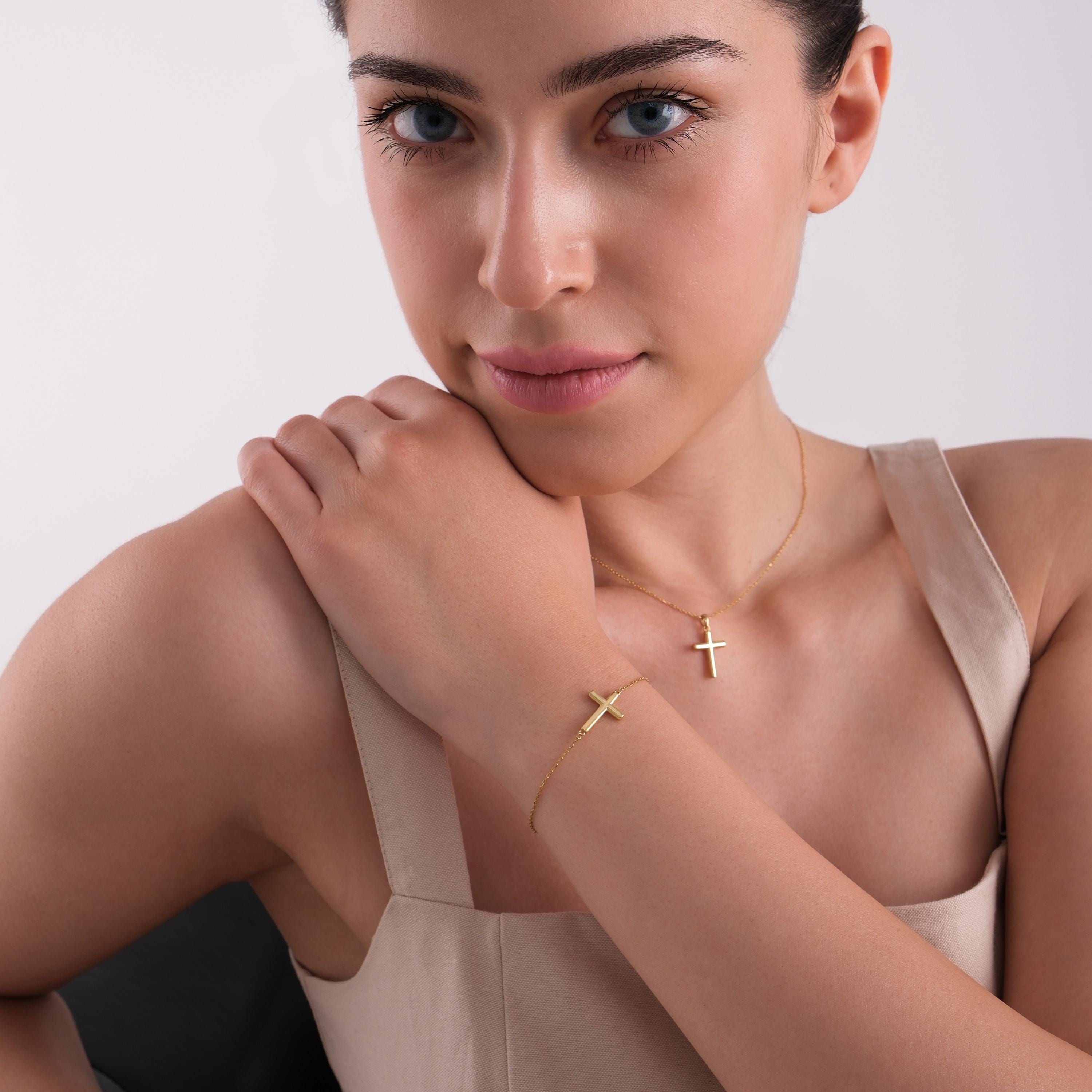 Woman wearing a matching set of 14K solid gold cross necklace and bold dainty cross bracelet, styled with a beige dress.