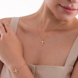 Woman wearing a minimalist 14K solid gold cross necklace and matching bracelet, styled with a beige sleeveless top.