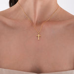 Close-up of a woman wearing a 14K solid gold cross necklace, centered on her upper chest with a soft natural light.