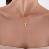 Close-up of a woman wearing a 14K solid gold cross necklace, centered on her upper chest with a soft natural light.