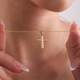 Close-up of a woman holding a delicate 14K solid gold cross necklace near her collarbone, highlighting the shiny pendant.