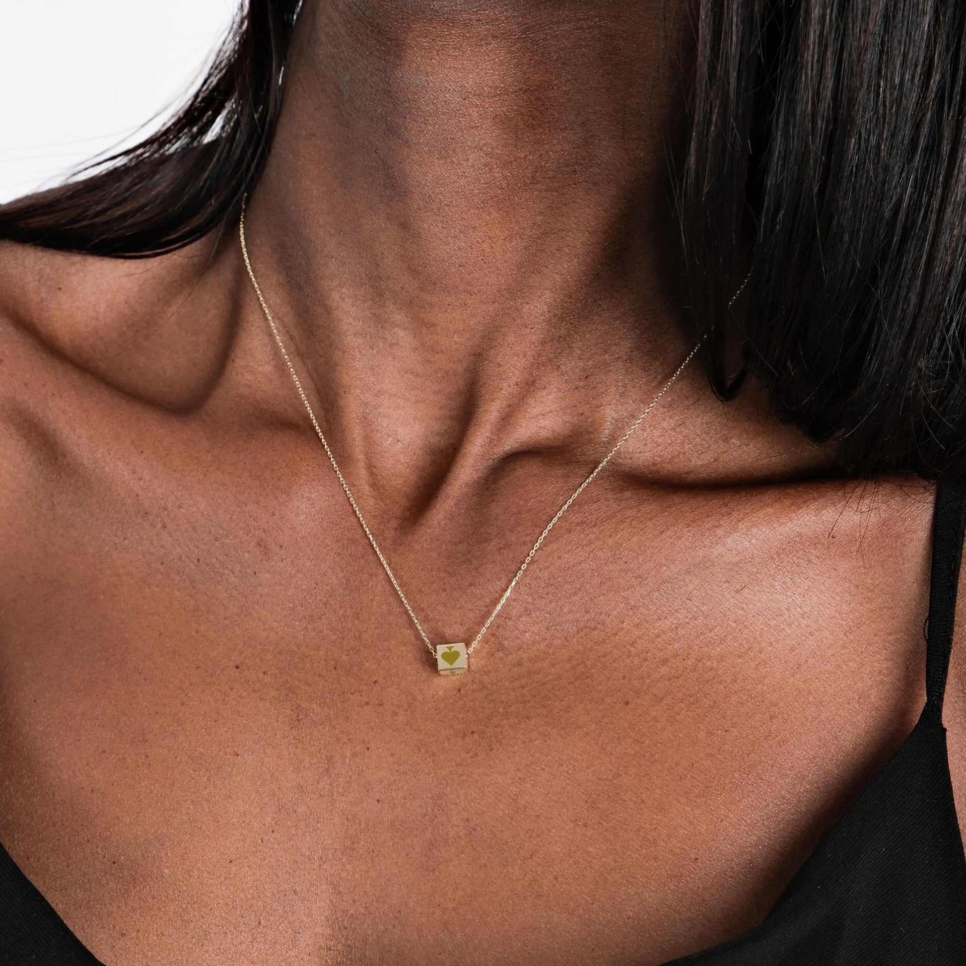 Minimalist 14K solid gold Spade Cards necklace worn by a woman in a black top, shown from the collarbone up.