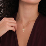 A woman wears the 18K Gold Vermeil Cross Necklace, holding the chain near her collarbone.
