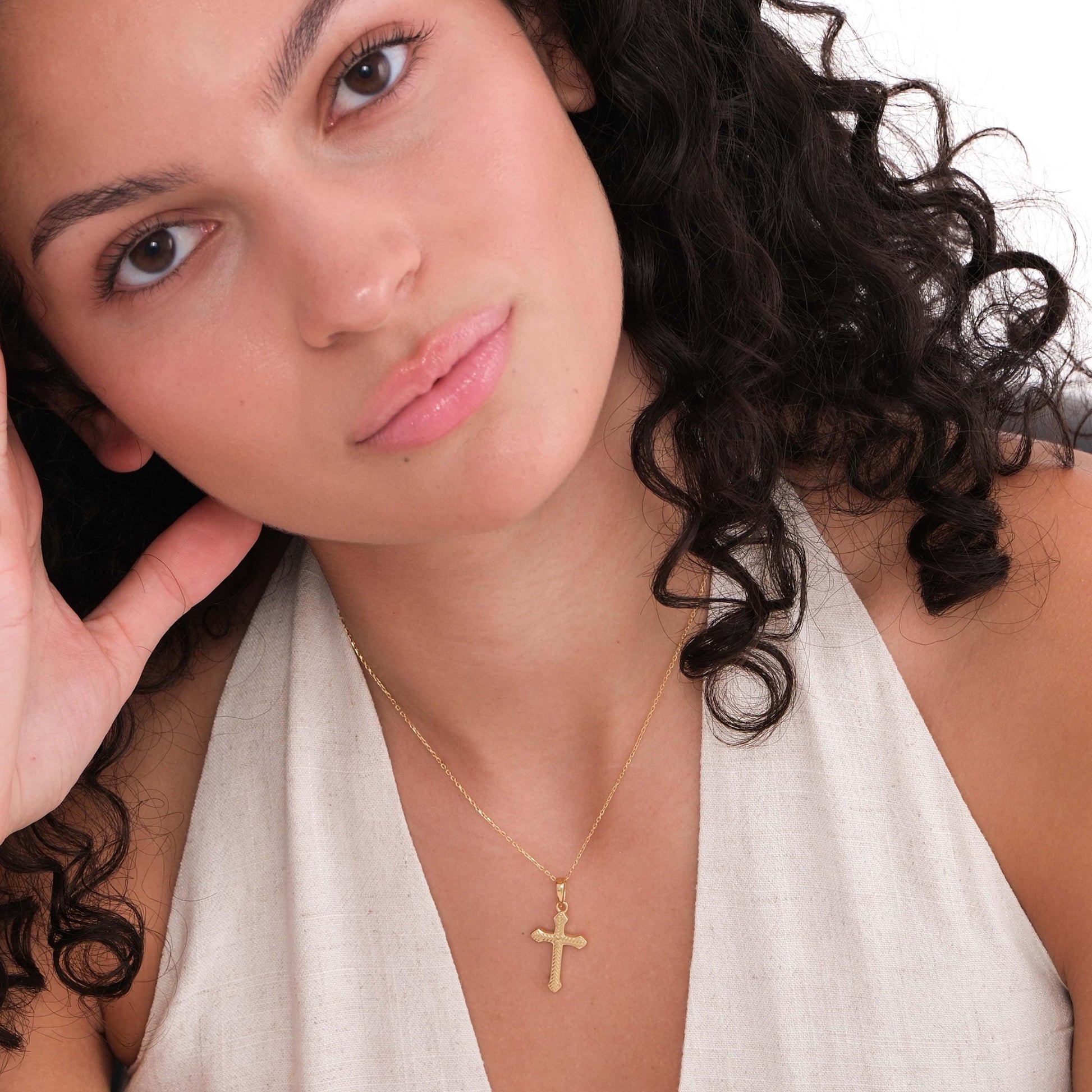 18K gold vermeil cross necklace for women styled with natural curls and a low-cut cream top.
